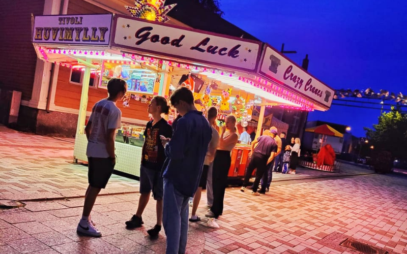 Tivolitunnelmaa illalla – valaistu pelikioski ja iloisia asiakkaita tapahtumassa
